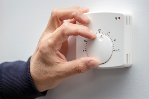 Hand touching heating dial on wall