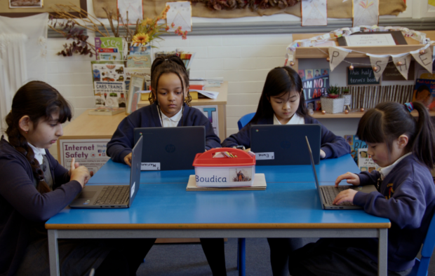 Four children sat at a desk on their laptops