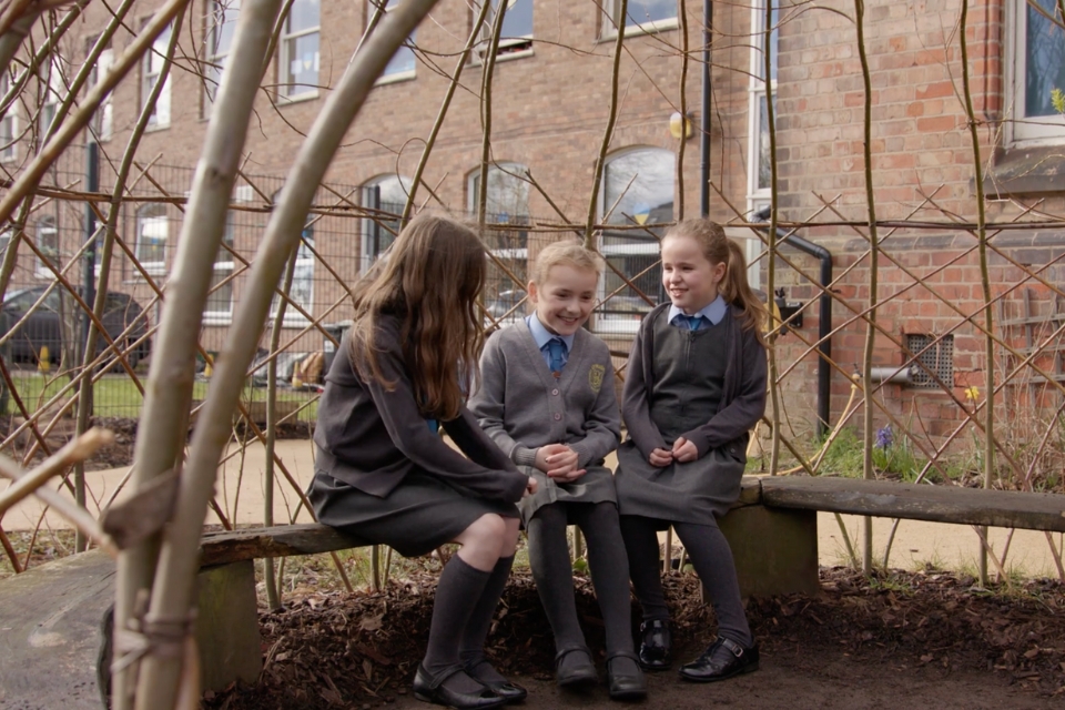 Three school children sat in a living willow dome
